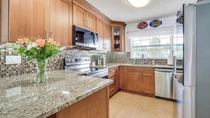 A kitchen with wooden cabinets, a granite countertop, a stainless steel refrigerator, and a window with a view of the outdoors. - Boat Dock & Kayaks: Canalfront Home in Homosassa (Homosassa)
