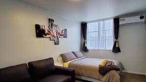 Een slaapkamer met een bed, een donkere bank en twee abstracte schilderijen aan de muur.