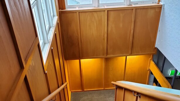 Een houten trap met bekleed landingsvlak en metalen leuning, die naar een hogere verdieping leidt.
