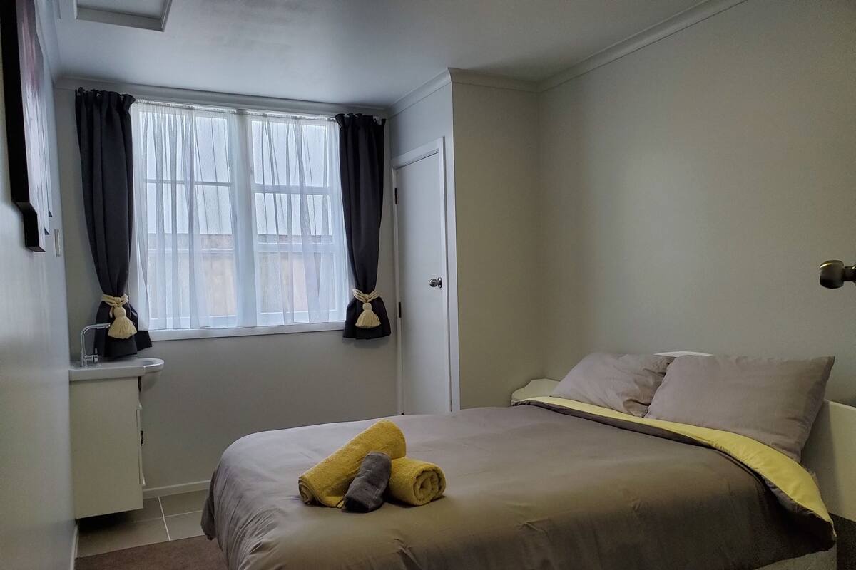 A bedroom with a bed, a window with curtains, a bedside table, and a lamp.