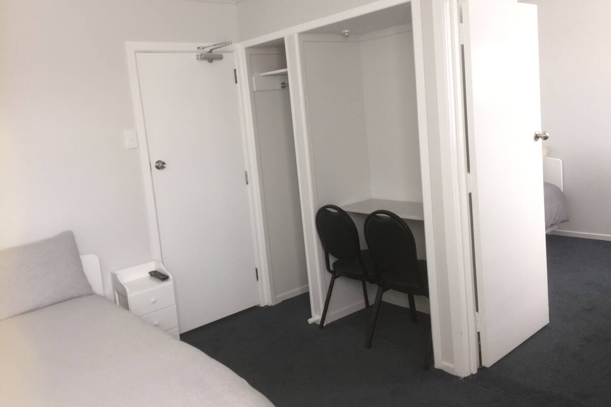 A bedroom with a bed, a desk, two chairs, and a wardrobe.