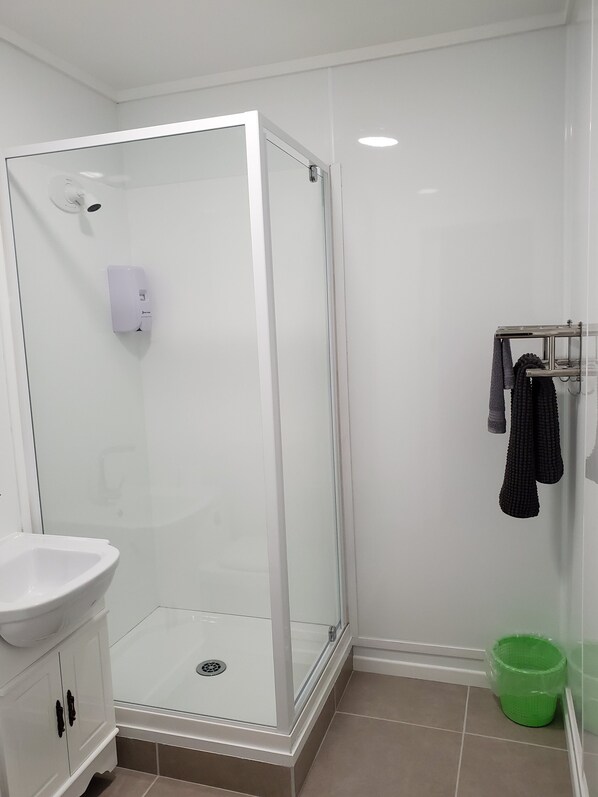 Un baño moderno con ducha envuelta en vidrio, un lavabo blanco y un cubo de basura verde.