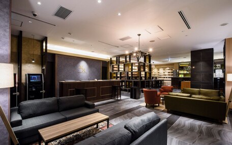 A modern hotel lobby with a reception desk, seating area, and bar.