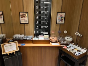 A hotel reception desk with a guest room directory, framed pictures, and a display of toiletries. - Meguro Holic Hotel (Tokyo)