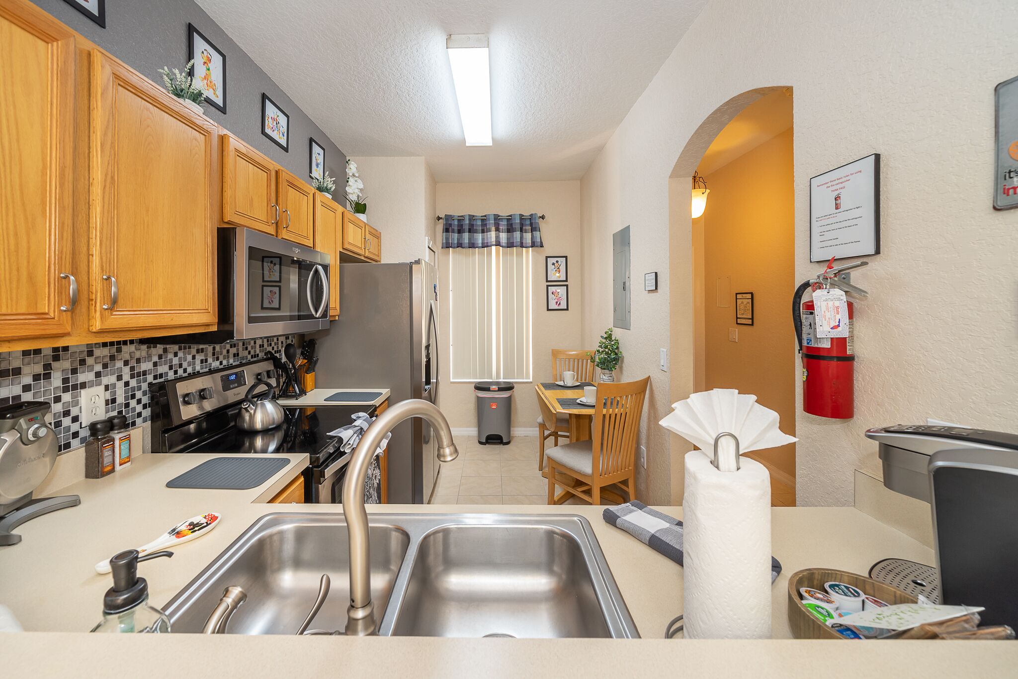 A compact kitchen with wooden cabinets, stainless steel appliances, and a small dining area with a table and chairs.