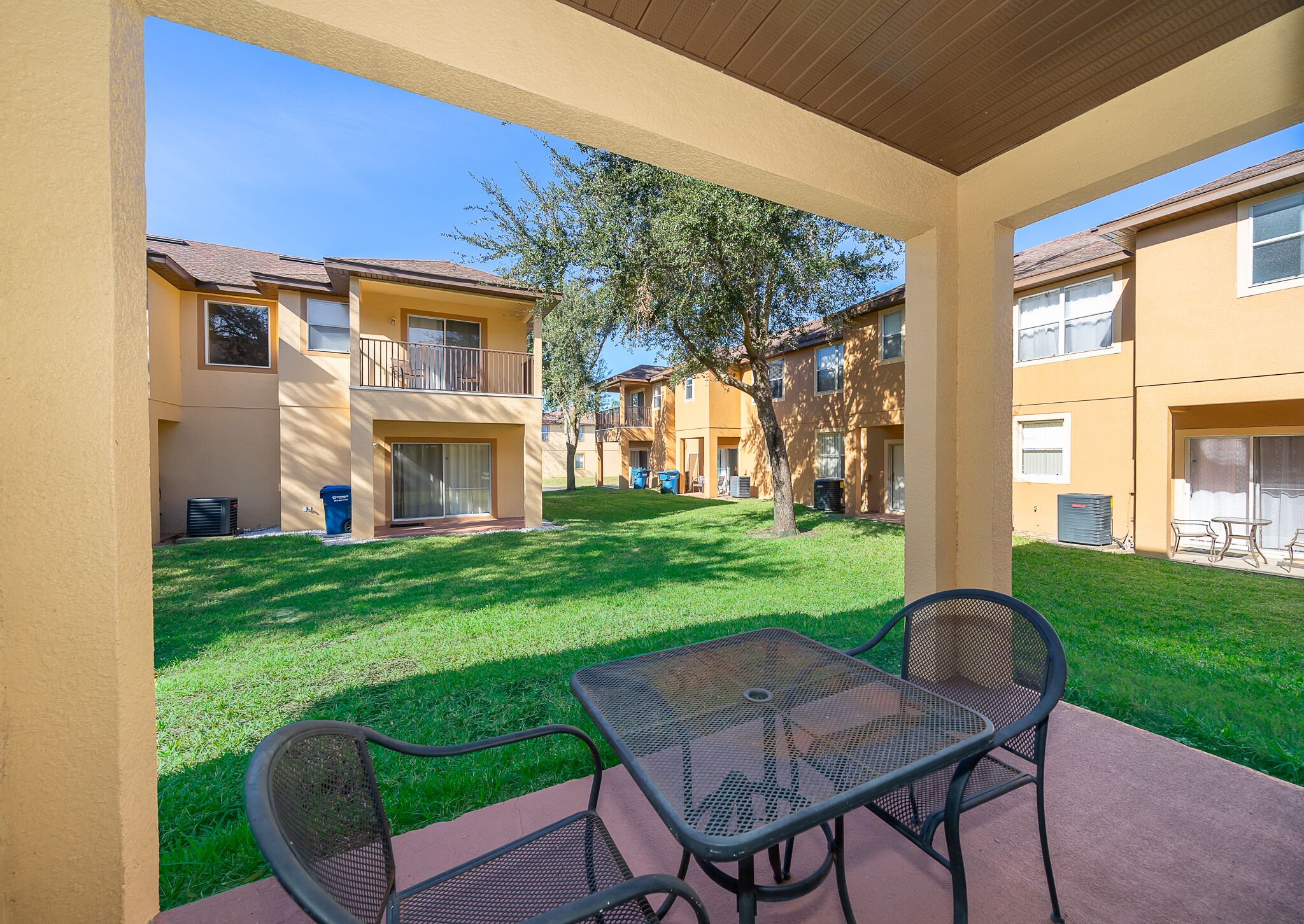An outdoor patio area with a table and chairs, surrounded by a well-maintained lawn and apartment buildings in the background.