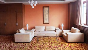 A hotel room with a large sofa set, a patterned carpet, a ceiling light fixture, and a wall-mounted artwork. - Avaunce Yabuli Hotel (Harbin)