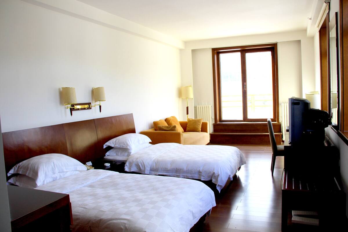 A hotel room with two beds, a sofa, a TV, and a window with a view.