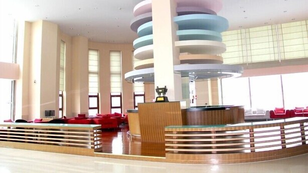 A lobby with a central reception desk, red seating, and a modern ceiling design. - Avaunce Yabuli Hotel (Harbin)