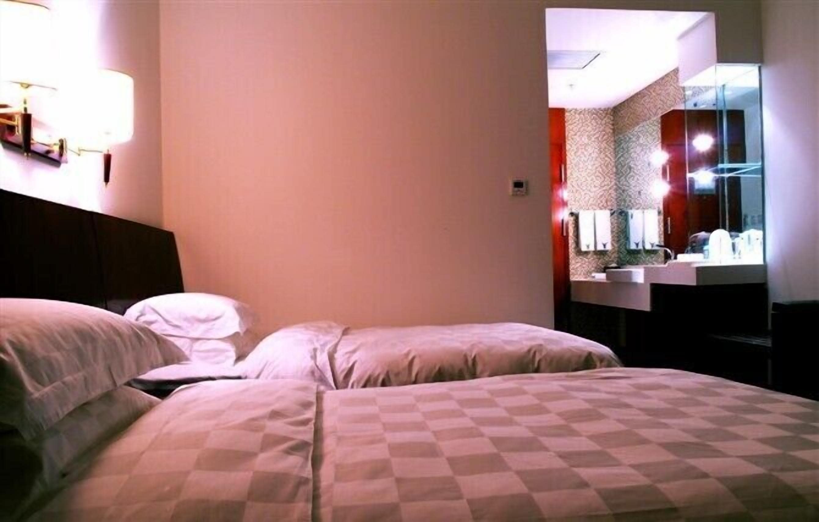 Habitación de hotel con dos camas, un espejo grande y un baño con lavamanos y espejo.