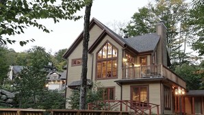 A two-story house with a balcony, large windows, and a wooden deck. - Chalet de luxe acceptant les animaux à louer CITQ 240284 (Stoneham-et-Tewkesbury)