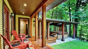 A wooden deck with red chairs and a table, a covered patio area, and a stone pathway leading to a wooden deck. - Chalet de luxe acceptant les animaux à louer CITQ 240284 (Stoneham-et-Tewkesbury)