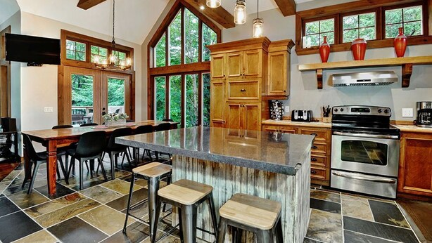 A spacious kitchen with a large island, wooden cabinets, and a stone tile floor. - Chalet de luxe acceptant les animaux à louer CITQ 240284 (Stoneham-et-Tewkesbury)