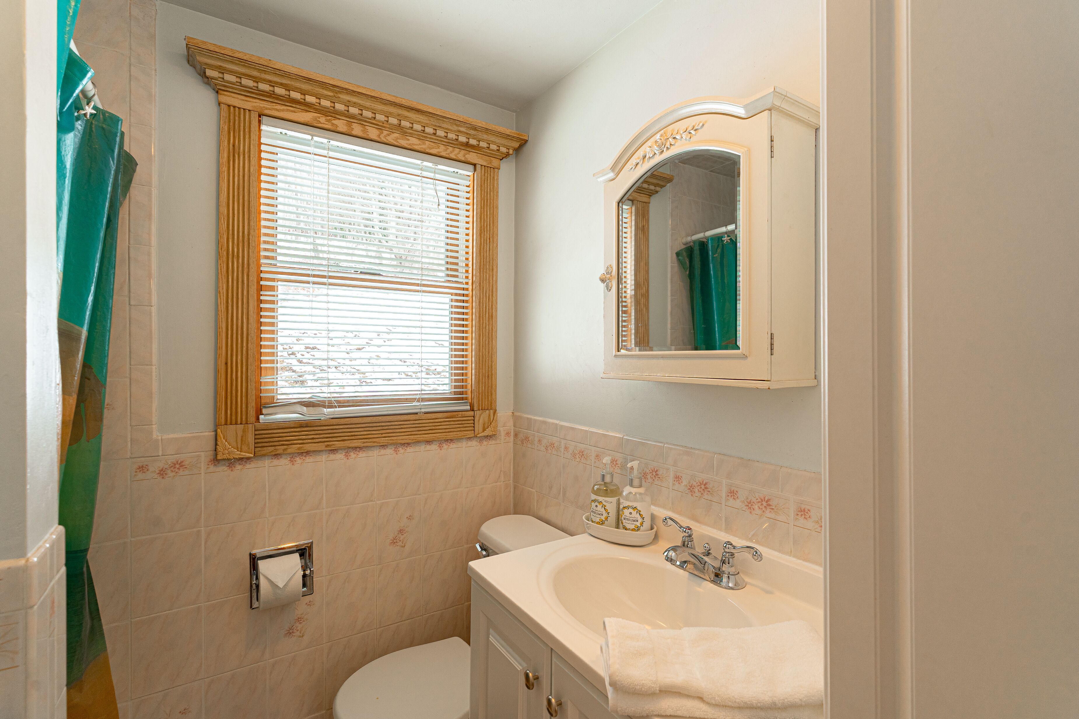 Une salle de bain avec des toilettes, un lavabo et une fenêtre équipée de stores.