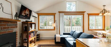 A cozy living room with a fireplace, a sofa, a dining table with wine glasses, and a TV mounted on the wall.