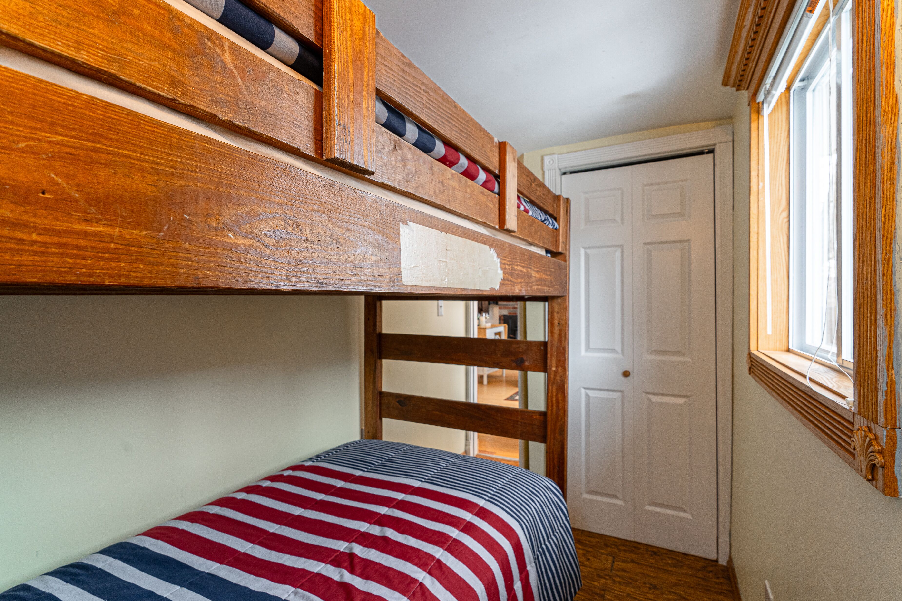A bunk bed with a striped bedspread, a wooden headboard, and a window with curtains.