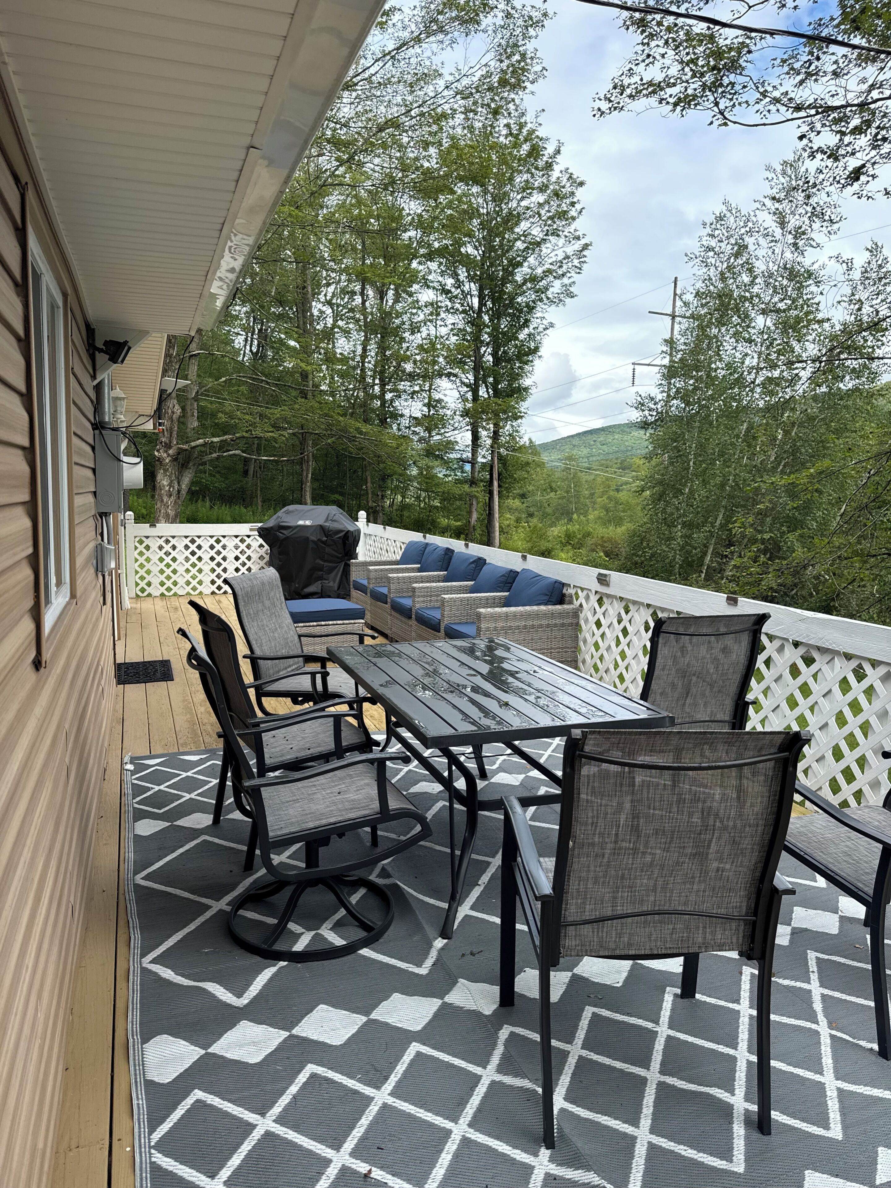 An outdoor patio with a table and chairs, a grill, and a view of the surrounding forest.