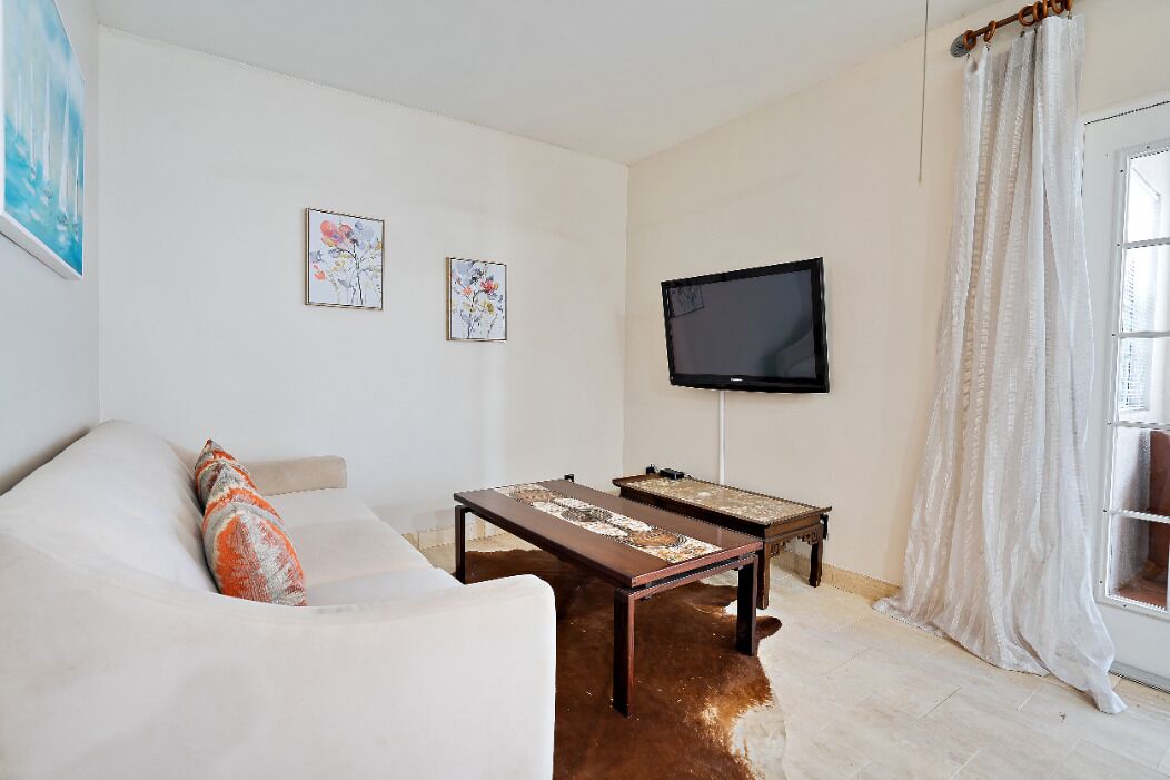 A living room with a sofa, two coffee tables, a flat-screen TV, and two framed artworks on the wall.