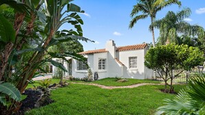 Une maison blanche avec un toit recouvert de tuiles rouges, entourée d’une végétation luxuriante et d’une pelouse bien entretenue.