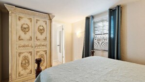 Une chambre avec un grand lit, une armoire classique et une fenêtre avec des rideaux.
