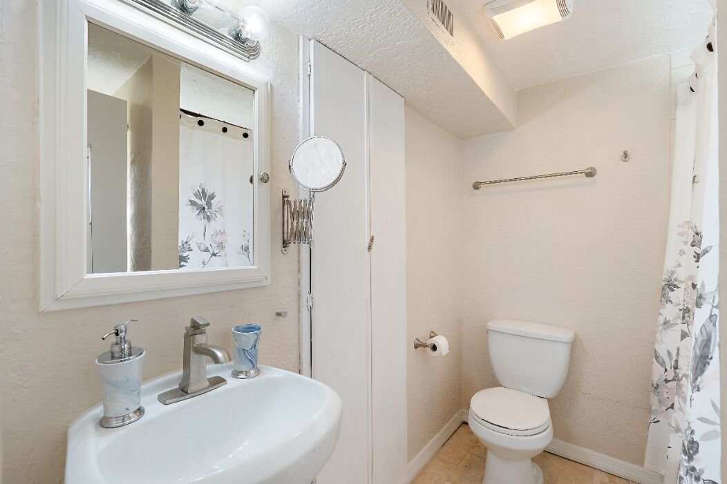 Un baño con un lavamanos blanco, un espejo, un inodoro y una cortina de ducha.