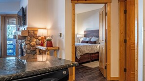 A kitchen with a dishwasher, a stone wall, and a wooden door leading to a bedroom with a bed and a nightstand. - Beautiful Views, Beautiful Condo , wifi, underground park, 1 minute to lifts (Copper Mountain)