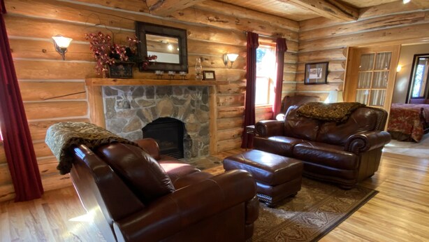 A log cabin interior with leather sofas, a stone fireplace, and wooden walls. - The Gingerbread Cottage - 2.5 acres, craft or meeting room (Bailey)