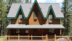 A log cabin with a steeply pitched roof, a front porch with a railing, and flower baskets on the windowsills. - The Gingerbread Cottage - 2.5 acres, craft or meeting room (Bailey)