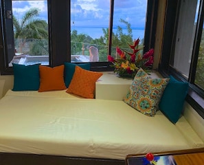 A room with a sofa bed, large windows, and a view of the ocean.