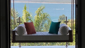 Una silla colgante con cojines, con vista al mar, palmeras y una costa distante.