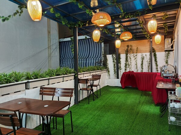 An outdoor dining area with tables and chairs, a red tablecloth, and hanging lanterns.
