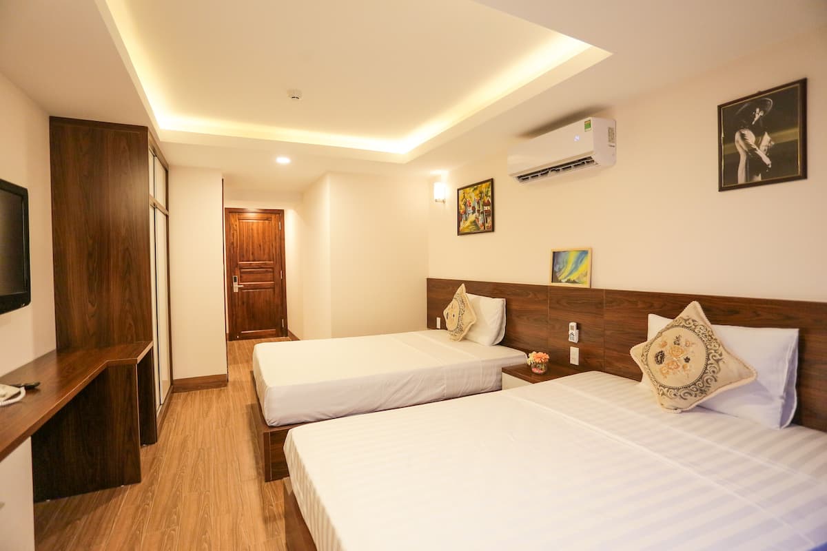 A hotel room with two beds, a desk, a TV, and an air conditioning unit.