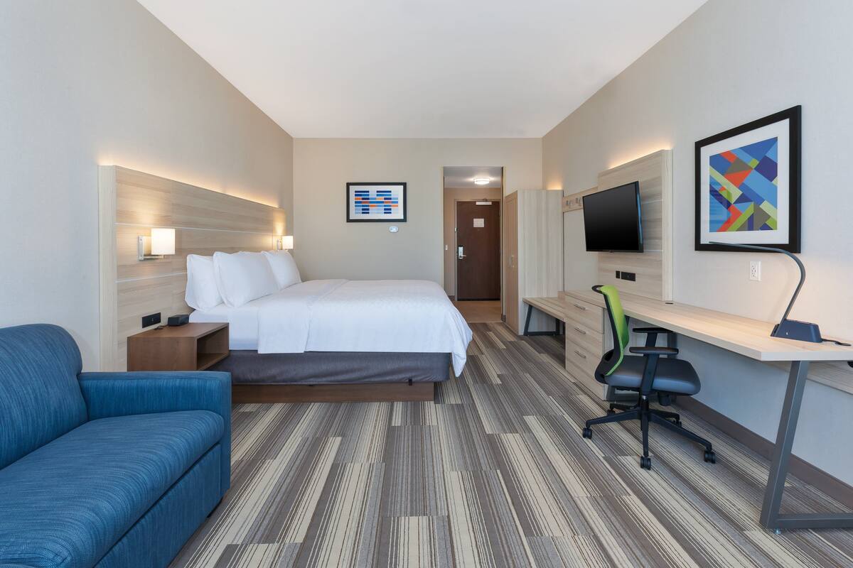 Habitación de hotel con cama, escritorio con silla, sofá, televisor y un cuadro en la pared.