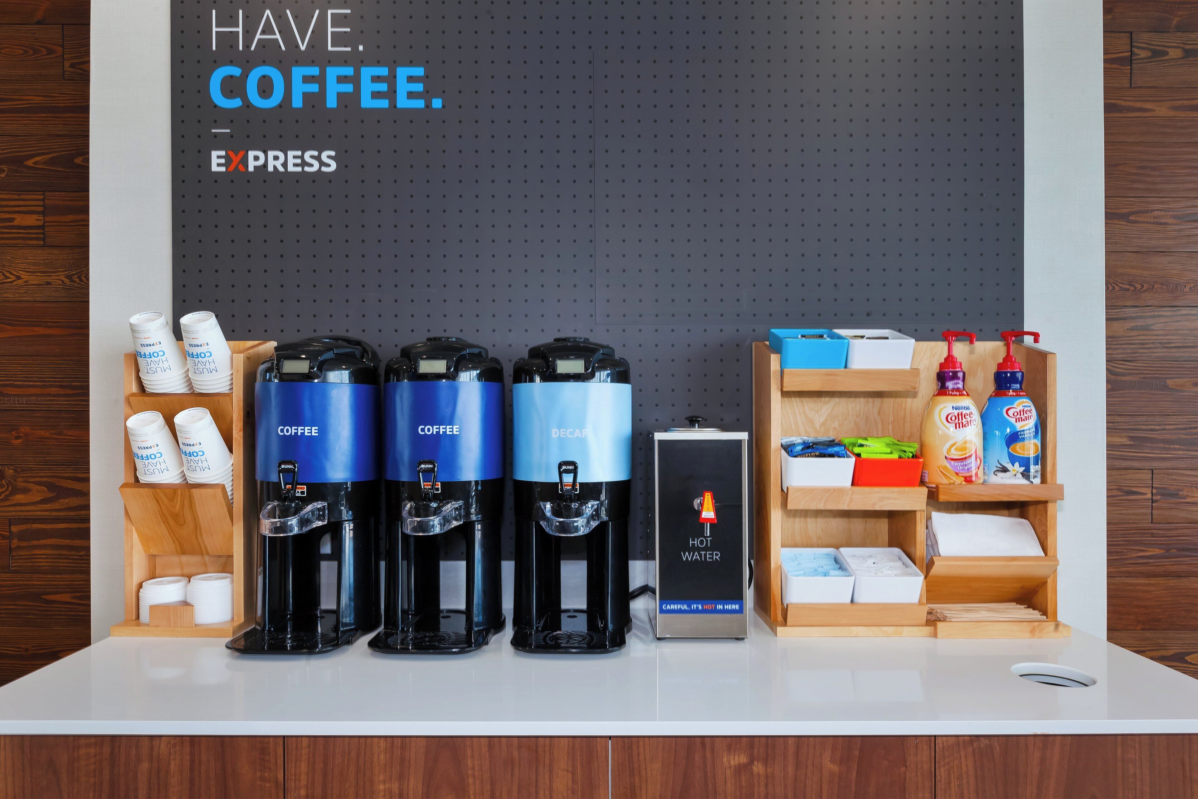 A coffee station with three coffee dispensers, a hot water dispenser, and a sign indicating hot water.