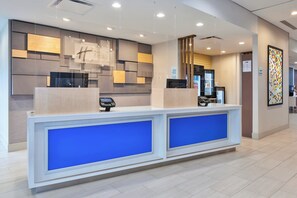 Una recepción de hotel con diseño moderno, que incluye un quiosco digital de registro y un separador de vidrio.