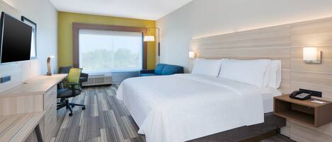 A hotel room with a large bed, a desk with a chair, a TV, and a window with a view of trees.