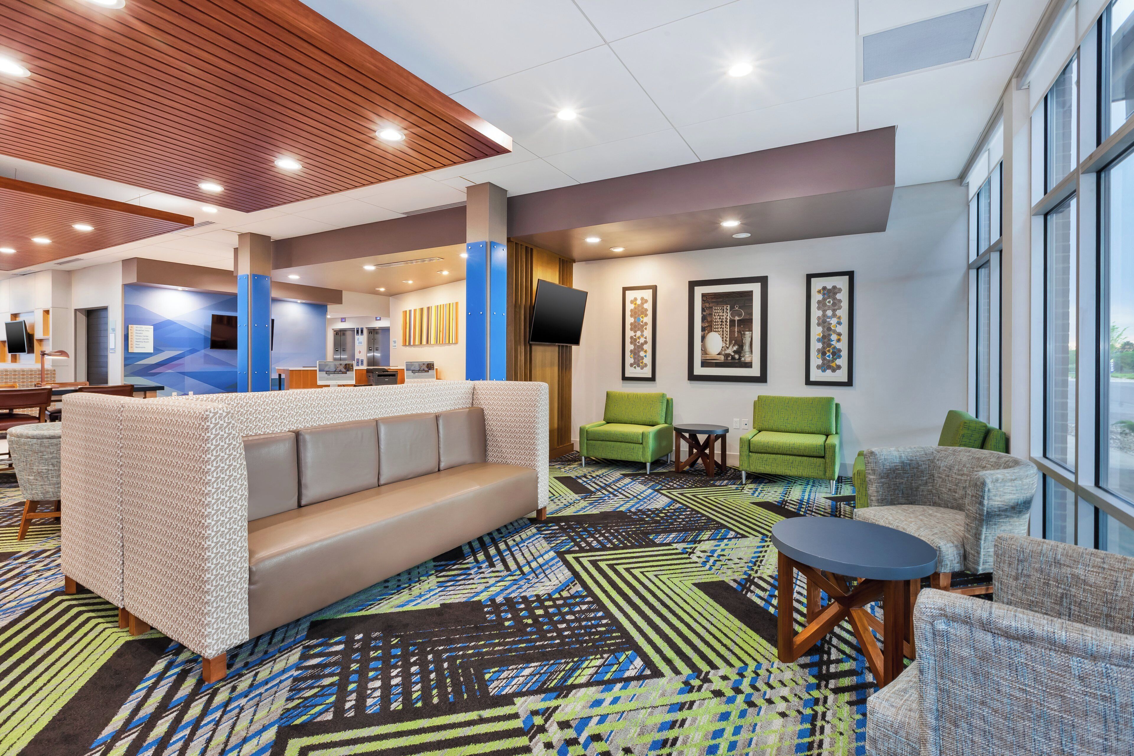A hotel lobby with a sofa, chairs, a patterned carpet, and artwork on the walls.