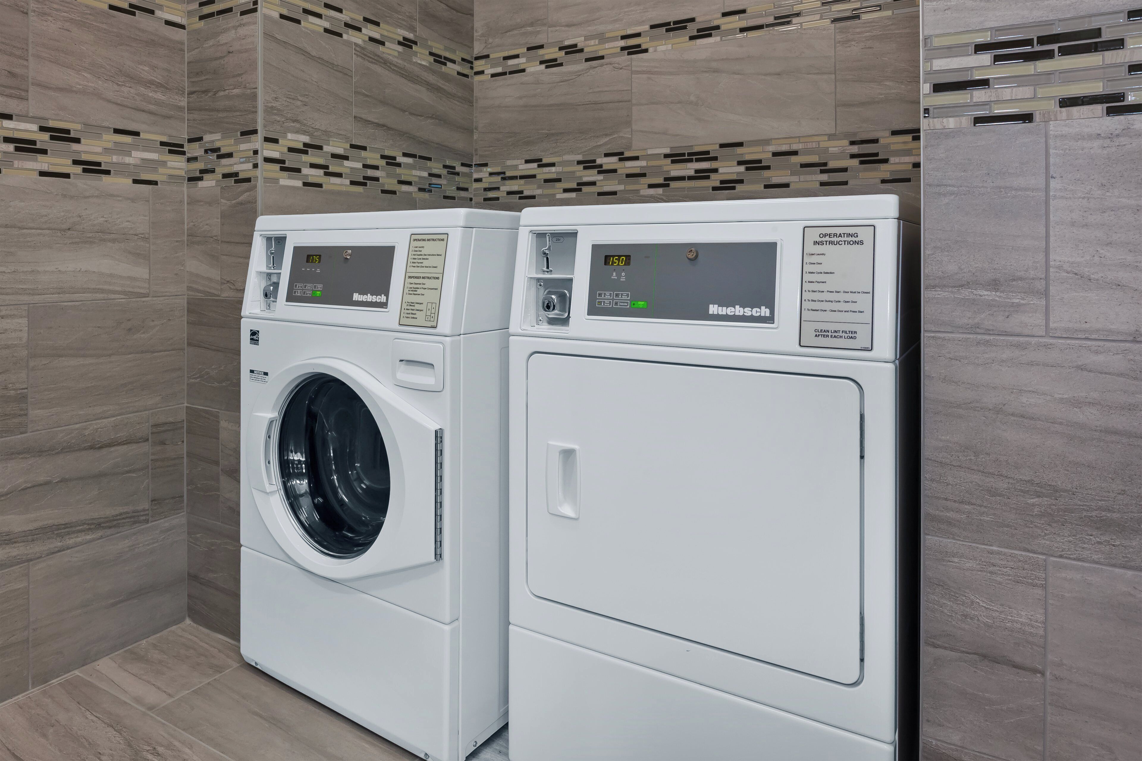 Two front-loading washing machines in a laundry room with tiled walls and a patterned backsplash.