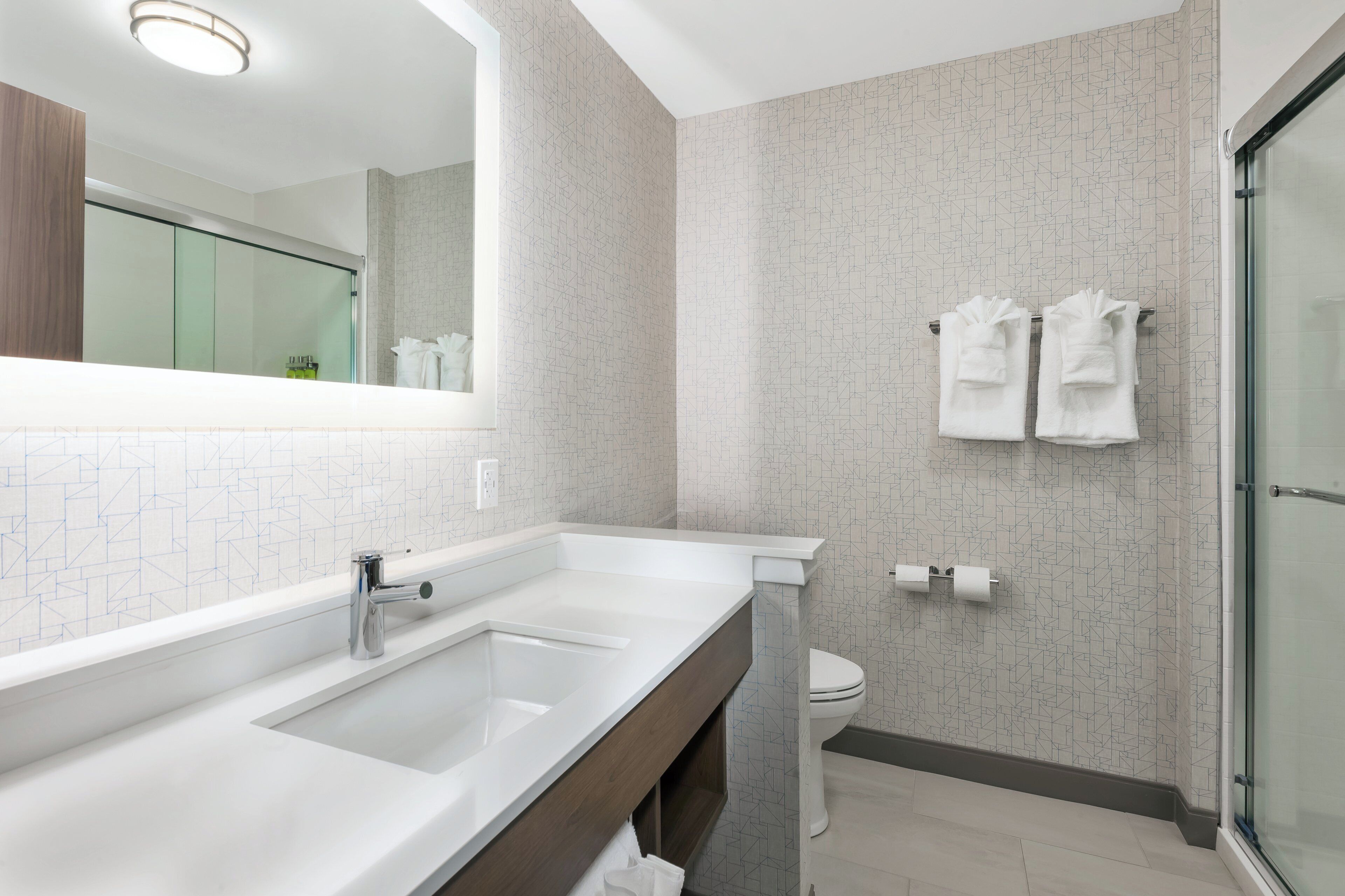 A modern bathroom with a large mirror, a double sink, a toilet, and a shower area.