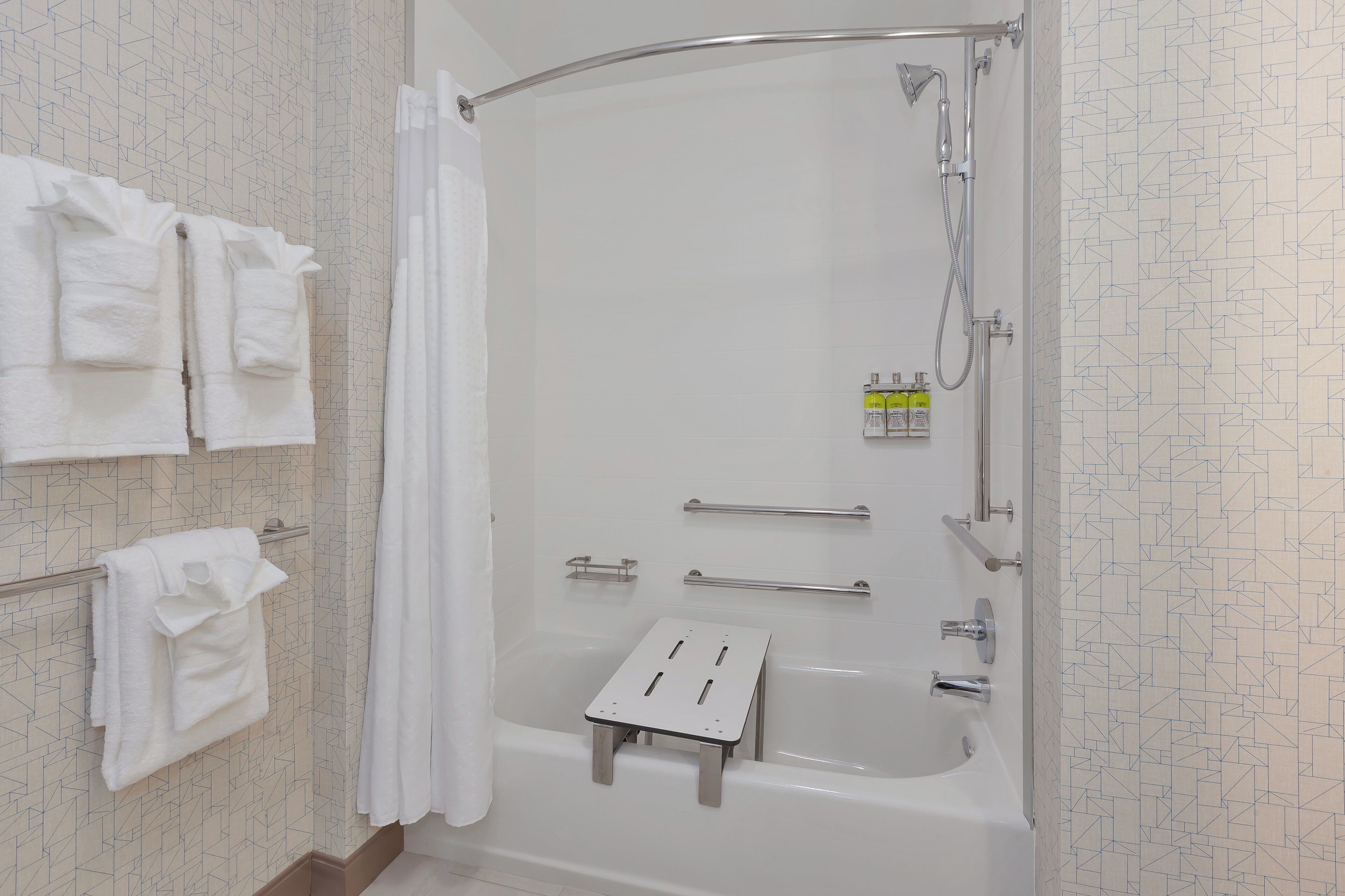 Un bagno moderno con una vasca, una doccia, un porta asciugamani e un piccolo sgabello.
