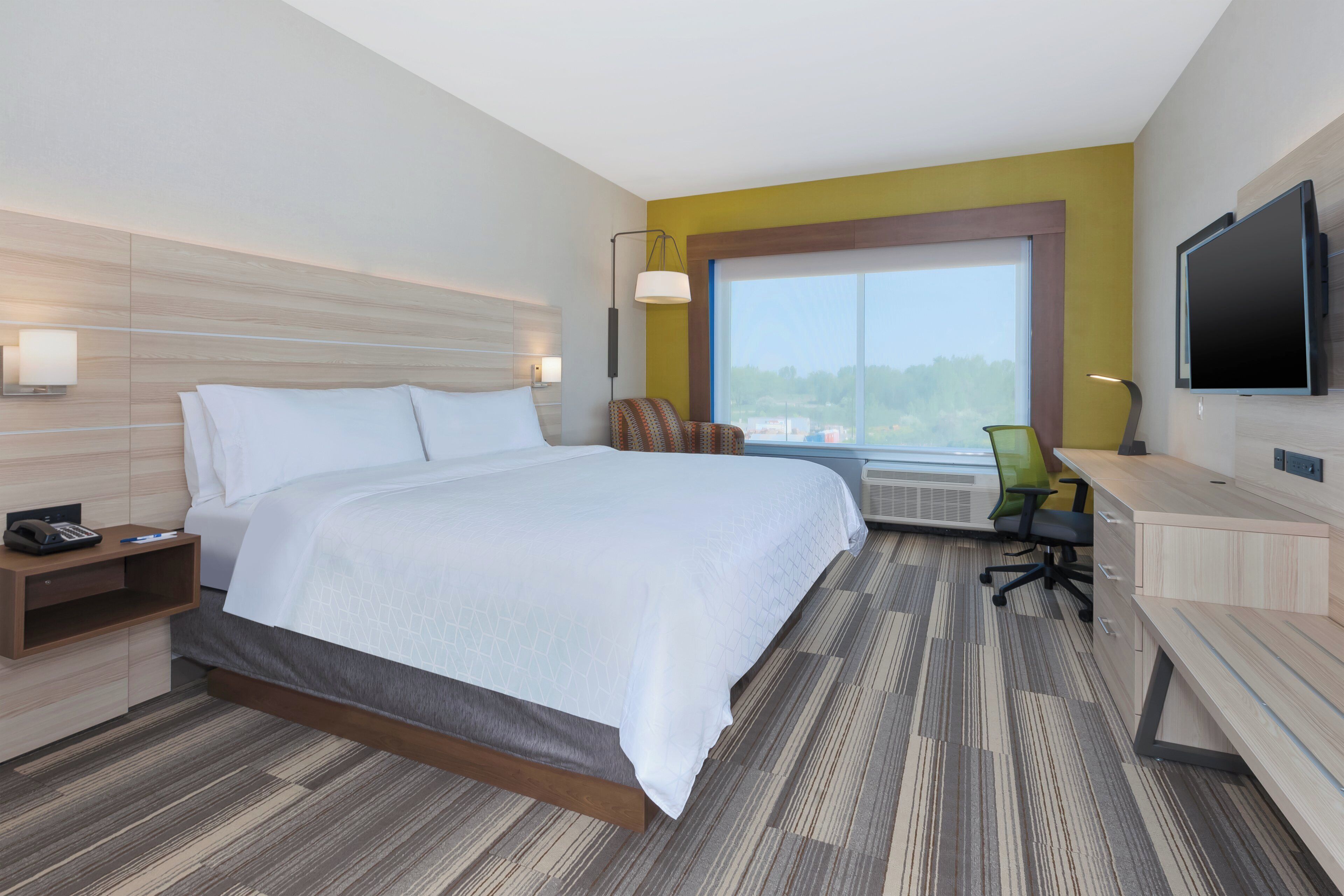 A hotel room with a bed, desk, chair, TV, and a large window.