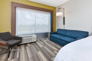 Una habitación de hotel con un ventanal grande, un sofá azul, un sillón gris y una cama blanca.