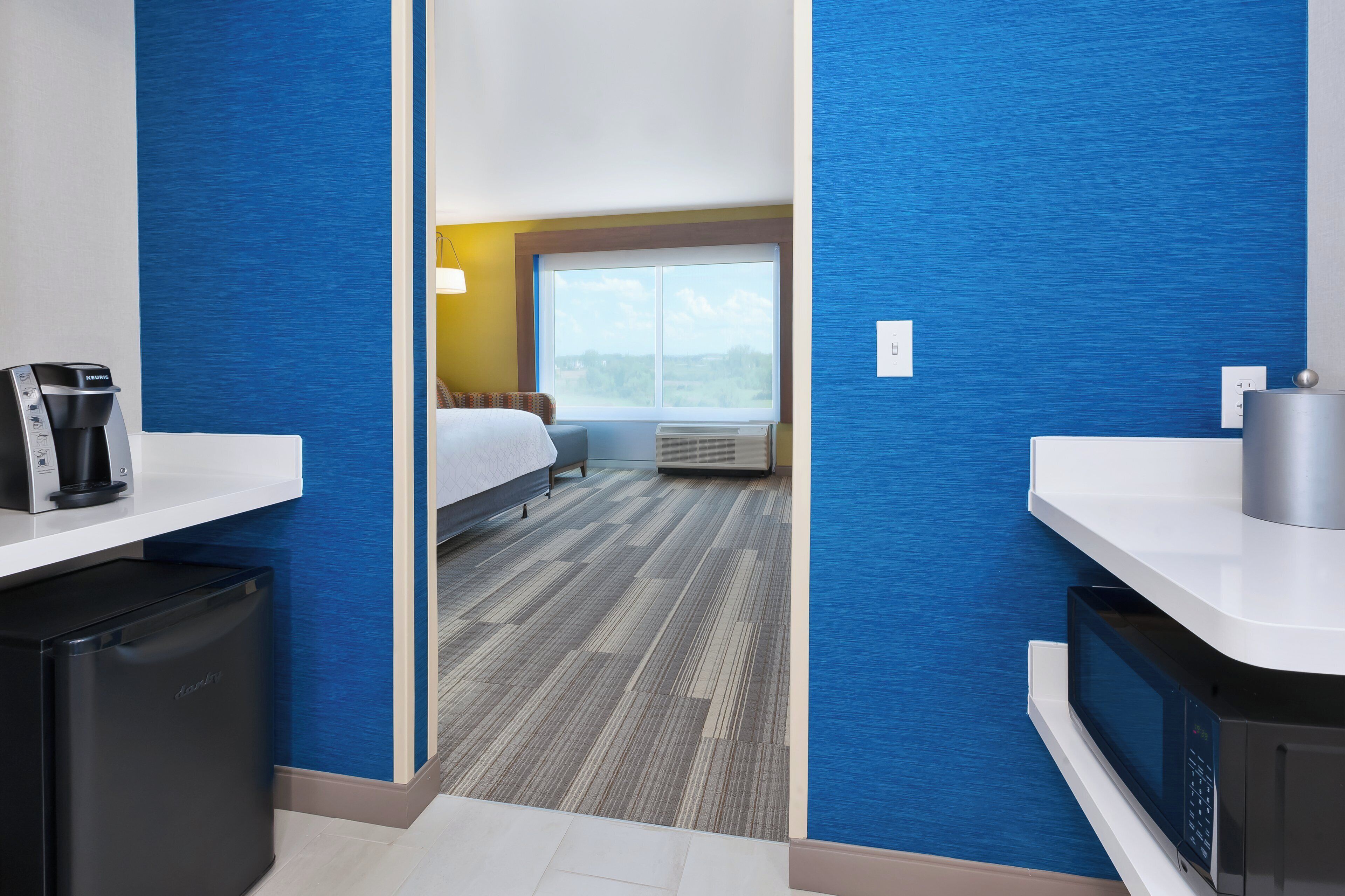 Habitación de hotel con cama, ventana, escritorio y cafetera, además de un microondas.