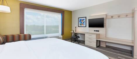 Habitación de hotel con una cama grande, un escritorio con computadora, un televisor y una ventana con vistas.