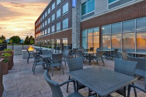 Un patio al aire libre con mesas y sillas, una chimenea y un edificio con grandes ventanales.
