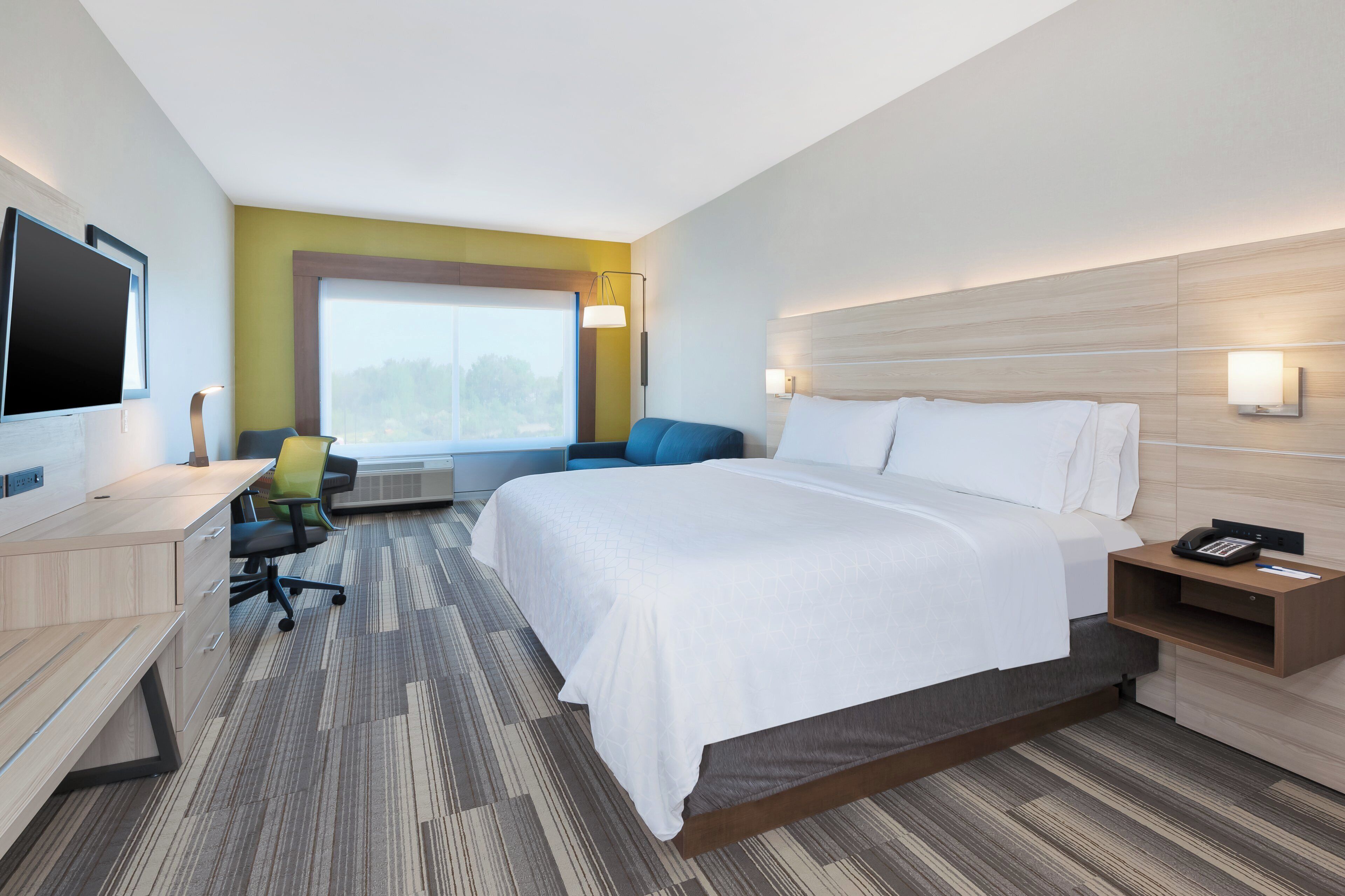 A hotel room with a bed, desk, chair, and a TV.