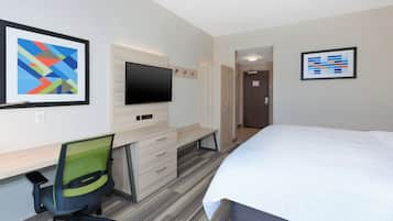 Habitación de hotel con cama, escritorio, silla, televisor y obras de arte en las paredes.