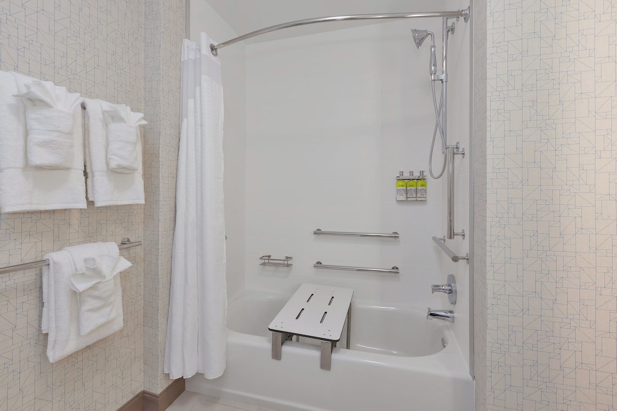 A modern bathroom with a bathtub, shower, towel rack, and a small step stool.