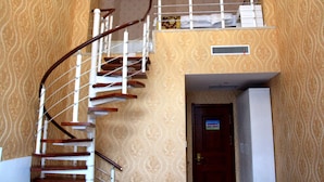 A spiral staircase with a wooden handrail and white balusters, leading to a landing with a white cabinet and a door with a sign. - Yabuli Skier Hotel (Harbin)