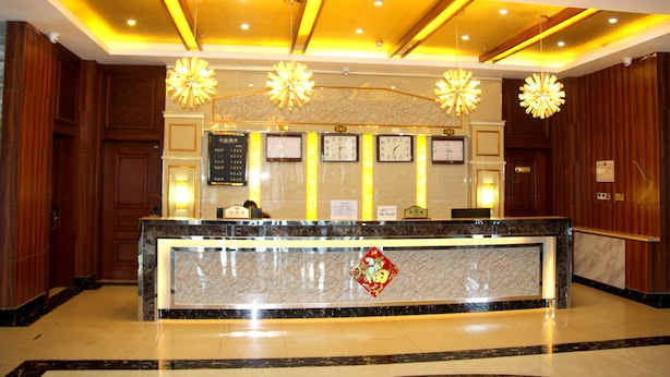 A hotel reception area with a marble counter, clocks, and decorative lighting fixtures. - Yabuli Skier Hotel (Harbin)
